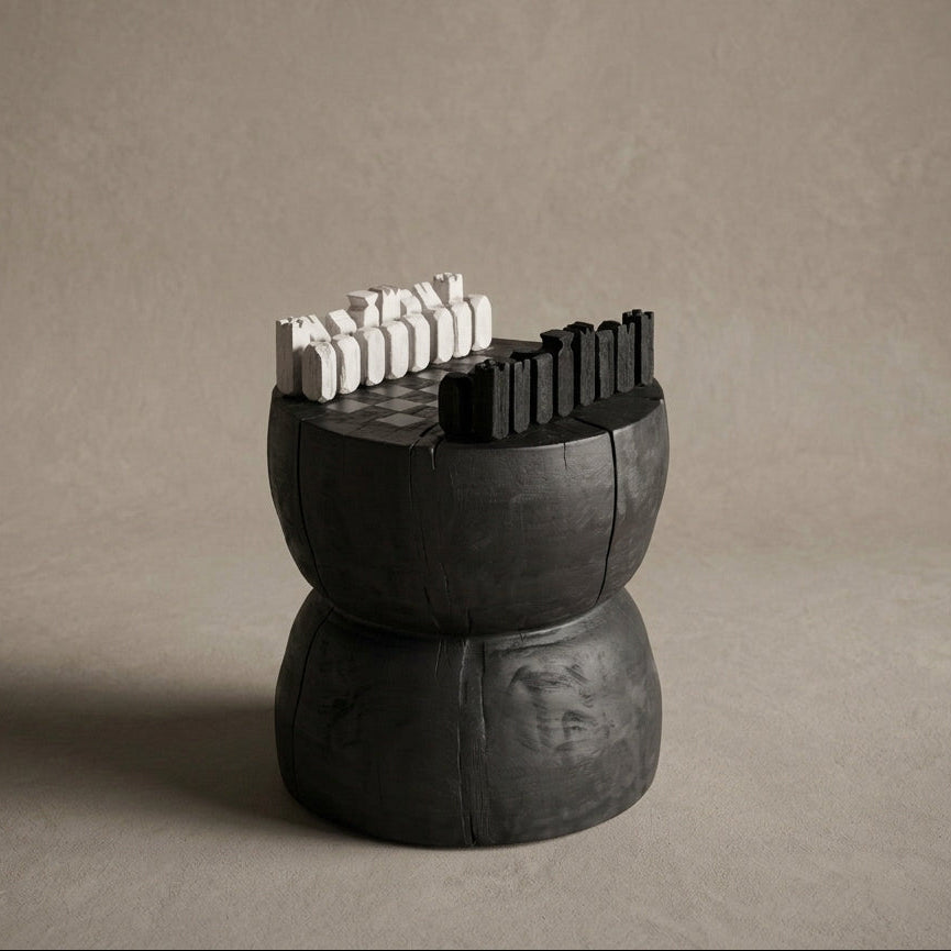 A sculptural black pedestal chess set with white and black chess pieces, photographed on a neutral textured beige background.